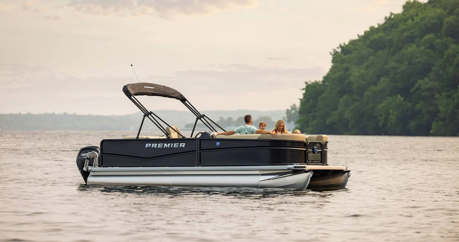 Family relaxing on a Premier pontoon near a wooded shoreline
